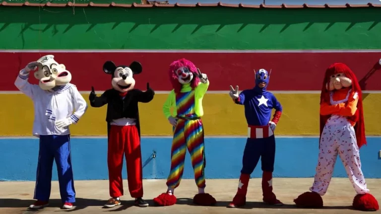 Grupo de personagens da Carreta Furacão posando em frente a uma parede colorida, com fantasias vibrantes e gestos divertidos.